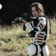 Rosita, clad in white Commonwealth armor, aims her assault rifle while standing in a field.
